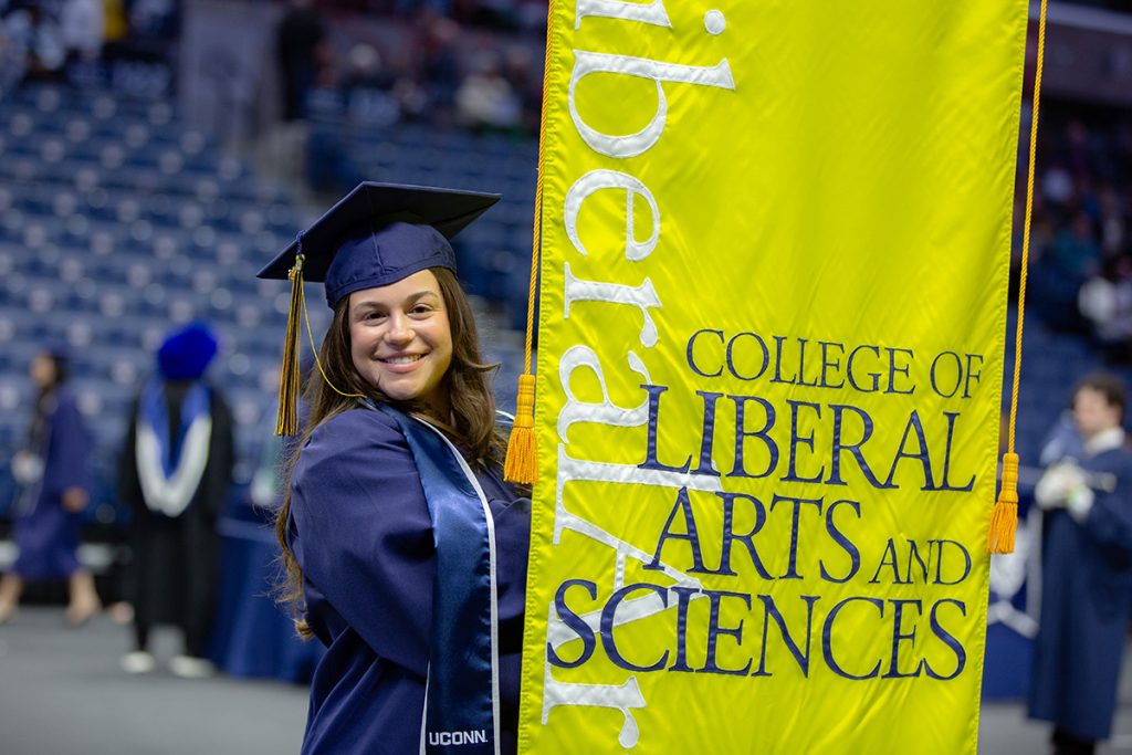 A graduate holds the yellow College of Liberal Arts and Sciences banner.