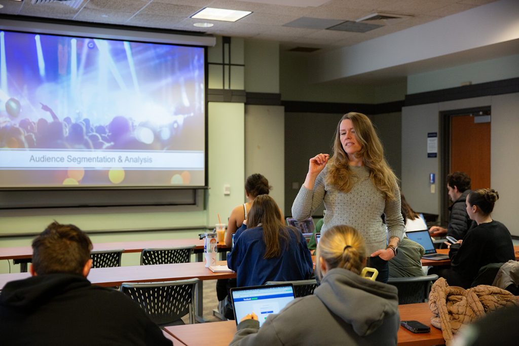 A professor stands in front of a projector during a communications class.